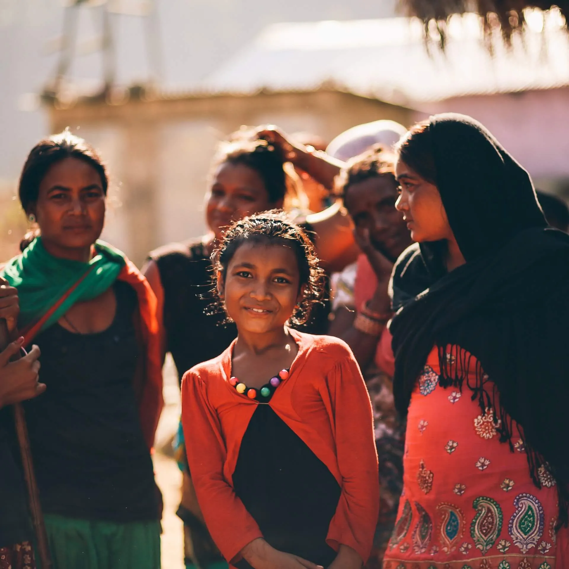 A girl smiling among women and children in a rural community.